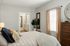 Inviting bedroom with soft lighting, cozy bed, decorative throw pillows, and plant accent. Natural light streams through large window with elegant curtains.