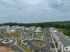 A stunning aerial view of a modern apartment complex surrounded by lush greenery, featuring multiple buildings, ample parking, and well-maintained landscaping.