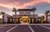 Elegant leasing office exterior with palm trees and warm sunset glow, inviting and modern design.