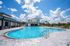 Inviting outdoor pool area with crystal-clear water, surrounded by stylish lounge chairs and vibrant orange parasols under a sunny blue sky.