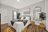 Inviting bedroom with modern decor, featuring a cozy blue and cream bed, elegant wood furniture, and a fresh plants near a full-length mirror.
