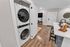 In-unit stacked washer and dryer located in a modern apartment, adjacent to an open-concept kitchen with wood-style flooring and contemporary finishes