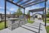 Chic outdoor barbecue area with stainless steel grill under a modern pergola, surrounded by lush greenery and palm trees, perfect for entertaining.