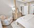 Elegant bedroom with a cozy floral armchair, wooden dresser with a round mirror, and soft ambient lighting, creating a tranquil retreat.