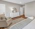 Inviting bedroom with elegant decor, featuring a plush armchair, dresser with mirror, and chic bedding on hardwood floors.