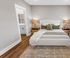 Elegant bedroom with a plush bed, cozy pillows, and warm lighting, leading to a modern bathroom through a sleek doorway.