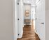 Bright hallway with elegant hardwood floors, featuring modern decor and a glimpse of a sunlit room in the distance.