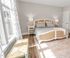Bright and inviting bedroom with stylish rattan bed, elegant side tables, and soft natural light from large windows.