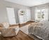Charming bedroom with elegant floral armchair, cozy bedding, and natural light streaming through stylish curtains.