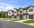 Contemporary townhouses with sleek architectural design, featuring two-story layouts, private garages, and lush green surroundings under a clear blue sky.