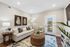 Chic living room with elegant beige sofa, vibrant botanical art, and cozy wicker accents, seamlessly connecting to outdoor space through stylish glass door.
