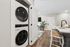 Modern apartment interior featuring a sleek stacked washer and dryer, open-concept kitchen with a stylish island, and a cozy living area adorned with a green plant and wall-mounted TV.