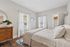 Inviting bedroom featuring cozy bedding, elegant dresser with mirror, and abundant natural light from large windows.