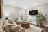 Inviting living room featuring plush beige sofas, a chic wicker coffee table, and a mounted flat-screen TV, creating a cozy and stylish ambiance.