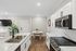 Chic modern kitchen with sleek white cabinets, stainless steel appliances, and elegant marble countertops, seamlessly transitioning into a cozy dining area with warm wood flooring.
