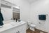 Modern bathroom with sleek white fixtures, elegant cabinetry, and stylish teal towel accents.