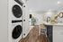 Modern apartment interior featuring a sleek stacked washer and dryer, elegant kitchen with a marble countertop, chic bar stools, and a cozy living area with stylish decor.