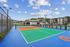 Modern outdoor sports court with vibrant blue and orange surfaces, surrounded by lush greenery and contemporary buildings under a clear blue sky.