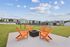 Inviting outdoor space with vibrant orange chairs surrounding a cozy fire pit, set against a backdrop of modern apartments and leisure facilities.