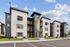 Modern apartment complex showcasing sleek architectural design with contrasting black and white exteriors and large windows, set against a bright blue sky.