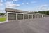 Spacious row of modern garages with sleek doors, situated in a well-maintained complex with lush greenery and a clear blue sky.