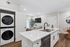 Modern open-concept kitchen with sleek marble countertop, integrated dishwasher, and stylish black faucet, adjacent to cozy living area and compact laundry closet.