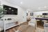 Elegant open-concept living space with a modern kitchen, stylish seating, natural decor, and a large wall-mounted TV.