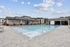 Inviting outdoor swimming pool with sleek, modern lounge seating and vibrant orange accents, surrounded by contemporary apartment buildings under a clear blue sky.