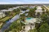 Aerial view of a luxurious apartment complex with a stunning pool, surrounded by lush greenery and a serene lake, offering a tropical oasis lifestyle.