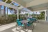 Charming outdoor patio with modern blue seating, shaded pergola, and built-in BBQ grill offering a relaxing, tropical vibe surrounded by palm trees.