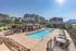 Charming apartment complex with a spacious outdoor pool, luxurious seating area, and mountain views under a clear blue sky.