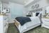 Elegant bedroom with modern decor, featuring a comfy bed with plush pillows, ornate wall art, and sleek white furniture.