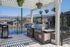 Charming outdoor grilling area with stainless steel barbecues under a pergola adorned with colorful hanging flowers.