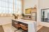 Modern kitchen with elegant marble island, warm leather chairs, and stainless steel appliances, bathed in natural light.