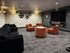 Chic media room with plush black sofas, vibrant orange chairs, and a large wall-mounted TV, perfect for entertainment.