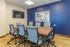 Contemporary meeting room with a sleek wooden table, ergonomic blue chairs, and vibrant blue accent wall featuring modern art.