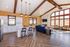 Luxurious open-concept living area featuring high vaulted ceilings with wooden beams, elegant pendant lighting, a chic kitchen with white cabinetry, and a cozy lounge area with large panoramic windows and stylish furnishings.