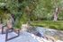 A photo of a picnic bench facing a flowing creek at the rear of the property. The bench is framed with vibrant green trees and gass on the opposing side of the creek.