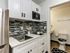 Modern compact kitchen with sleek stainless steel fridge, stylish backsplash, and white cabinetry, adjacent to pristine bathroom.
