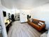 Modern living room with elegant decor, featuring a sleek leather sofa, stylish shelving, and a cozy open-plan kitchen.