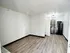 Bright and modern apartment interior with sleek wood flooring, showcasing an open layout leading to a compact kitchen with contemporary cabinetry and stainless steel appliances.