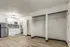 Studio apartment interior at Fusion at Rye in Houston Texas showing an open space with wood style flooring, two open closets with hanging rods, a small kitchenette with white cabinets, stainless steel refrigerator, microwave, tiled backsplash, and a doorway leading to the bathroom.