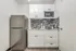 Small studio kitchen at Fusion at Rye Apartments in Houston Texas featuring a stainless steel refrigerator, white upper and lower cabinets, a microwave, a single basin sink, and a gray tile backsplash with mixed pattern tiles.