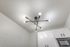 Close up view of a ceiling light fixture at Fusion at Rye Apartments in Houston Texas showing a modern multi arm design with exposed bulbs and brass accents, positioned above white kitchen cabinets and a microwave.