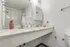 Bathroom sink area at Fusion at Rye Apartments in Houston Texas showing a wide countertop with a marble style surface, a chrome faucet, soap and lotion dispensers, a mounted medicine cabinet, a wall outlet with a charging device, a towel bar, and part of the shower curtain and toilet visible.