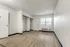 Unfurnished studio room at Fusion at Rye Apartments in Houston Texas showing wood style flooring, two open closets with hanging rods and wire shelves, a white entry door, a large window with blinds, and an in room air conditioning unit below the window.