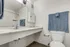 Bathroom at Fusion at Rye Apartments in Houston Texas showing a wide marble style countertop with a chrome faucet, a large wall mirror, a mounted medicine cabinet, a white toilet, a towel bar with blue towels, and part of the shower area with a curtain and shower rod.