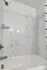 Studio bathroom tub and shower with modern fixtures and marble-style wall panels at The Reserve at Rye 290.