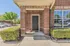 Charming brick exterior of a modern apartment entrance, featuring a welcoming path with vibrant greenery and sunny surroundings.