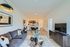 Modern living space featuring a cozy gray sofa, elegant decor, and an open-concept kitchen with sleek cabinetry and bar seating.